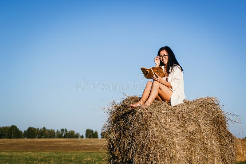 A menina bronzeada senta-se em um monte de feno fotos de stock royalty free A menina bronzeada senta-se em um monte de feno fotos de stock royalty free