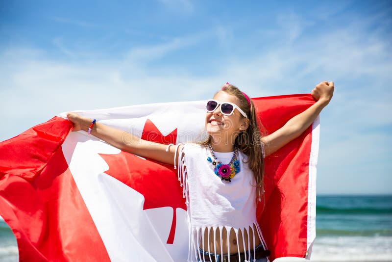 A menina canadense feliz leva a bandeira vermelha branca de vibração de Canadá contra o fundo do céu azul e do oceano foto de stock royalty free A menina canadense feliz leva a bandeira vermelha branca de vibração de Canadá contra o fundo do céu azul e do oceano foto de stock royalty free