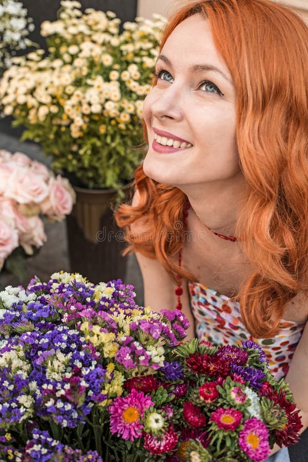 Menina caucasiano do ruivo bonito que cheira flores coloridas no jardim imagem de stock Menina caucasiano do ruivo bonito que cheira flores coloridas no jardim imagem de stock