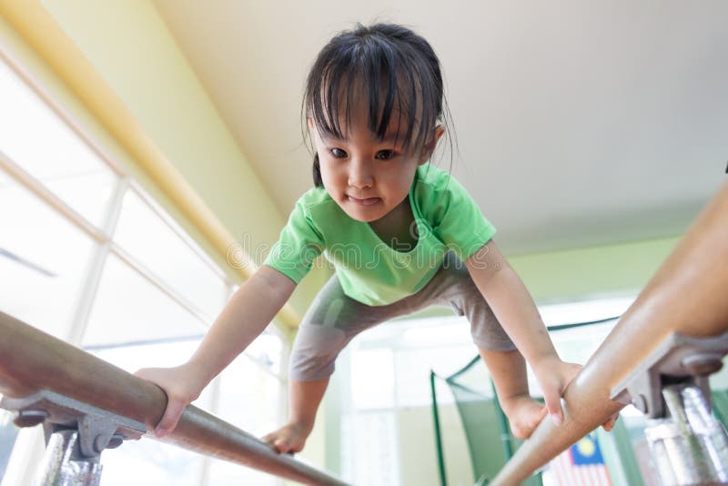 Menina chinesa asiática que escala em barras paralelas imagem de stock Menina chinesa asiática que escala em barras paralelas imagem de stock
