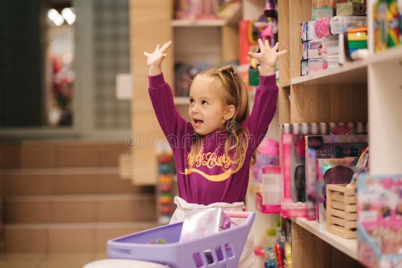Menina com carrinho de compras pequeno no shopping infantil Garota feliz escolhendo o que comprar na loja de brinquedos imagem de stock Menina com carrinho de compras pequeno no shopping infantil Garota feliz escolhendo o que comprar na loja de brinquedos imagem de stock