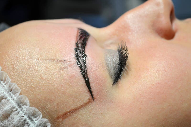 Menina com a composição que encontra-se no tampão estéril no procedimento de microblading com a uma sobrancelha terminada fotografia de stock Menina com a composição que encontra-se no tampão estéril no procedimento de microblading com a uma sobrancelha terminada fotografia de stock