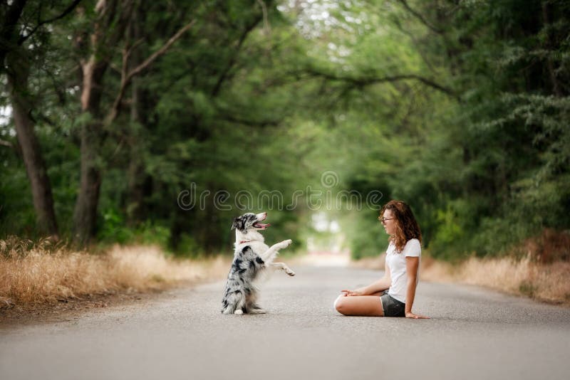 A menina com cão senta-se na estrada na floresta o cão faz um truque fotografia de stock A menina com cão senta-se na estrada na floresta o cão faz um truque fotografia de stock