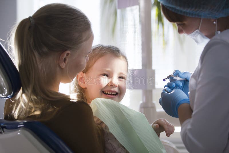 Menina com a mamã na cadeira do dentista - a criança está sorrindo imagem de stock Menina com a mamã na cadeira do dentista - a criança está sorrindo imagem de stock
