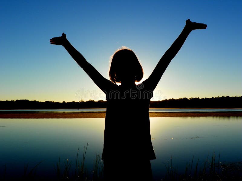 A silhouette of a girl with her arms raised to heaven standing in front of a lake. A silhouette of a girl with her arms raised to heaven standing in front of a lake.