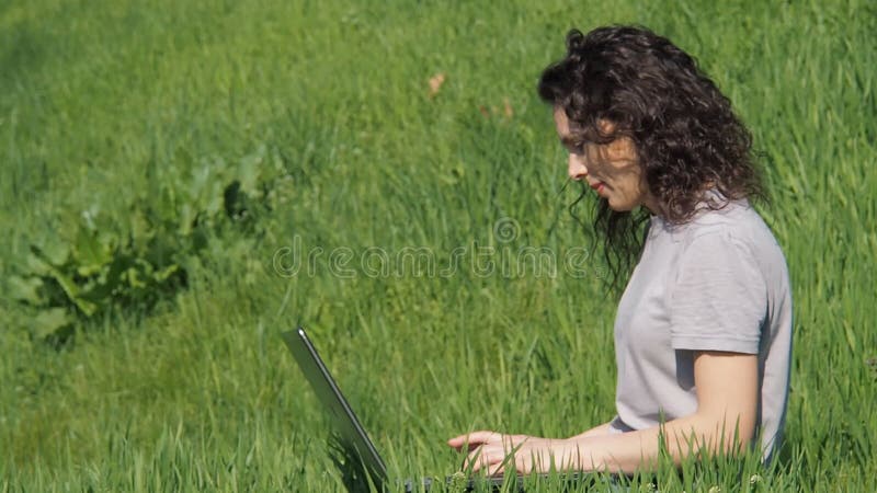 Menina com um portátil Menina na grama verde com portátil Jovem mulher em um parque em um dia ensolarado