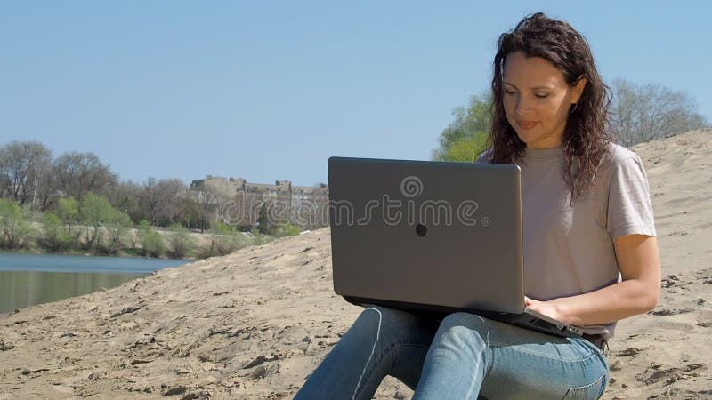 Menina com um portátil pela água Trabalhe no computador no ar fresco pelo rio Dia ensolarado da mola na natureza