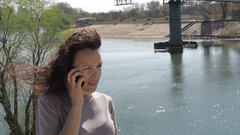 Menina com um telefone pelo rio Com o móbil no ar fresco perto da água Dia ensolarado na natureza