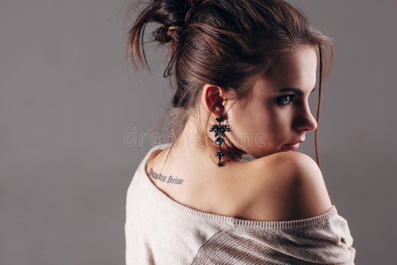 A menina com uma tatuagem que esteja olhando para trás através de um ombro