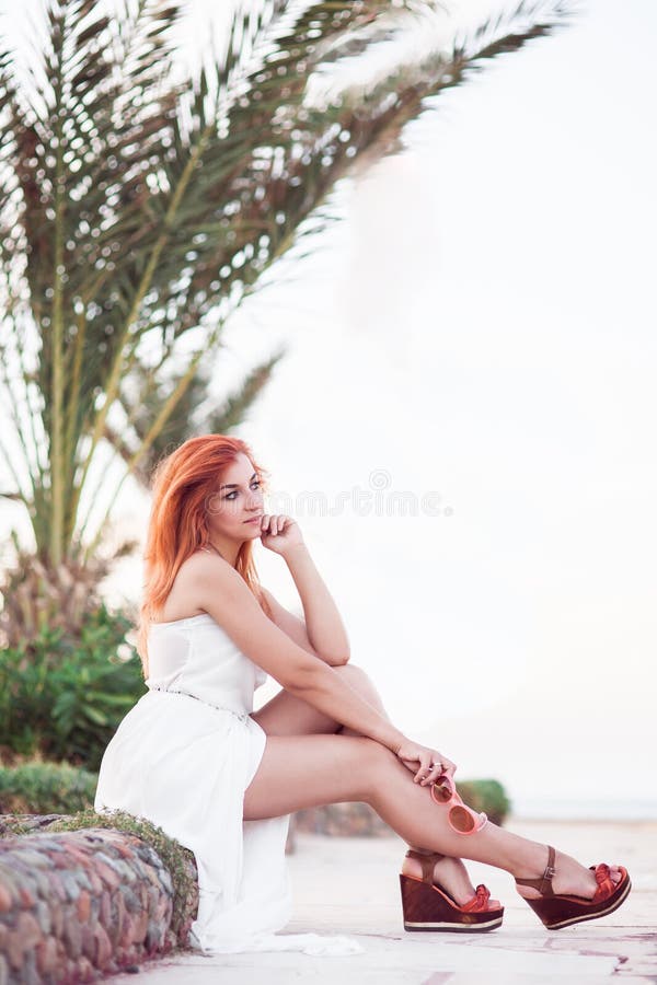 Menina da beleza no vestido branco do verão que senta-se em um pavimento de pedra fotografia de stock royalty free Menina da beleza no vestido branco do verão que senta-se em um pavimento de pedra fotografia de stock royalty free