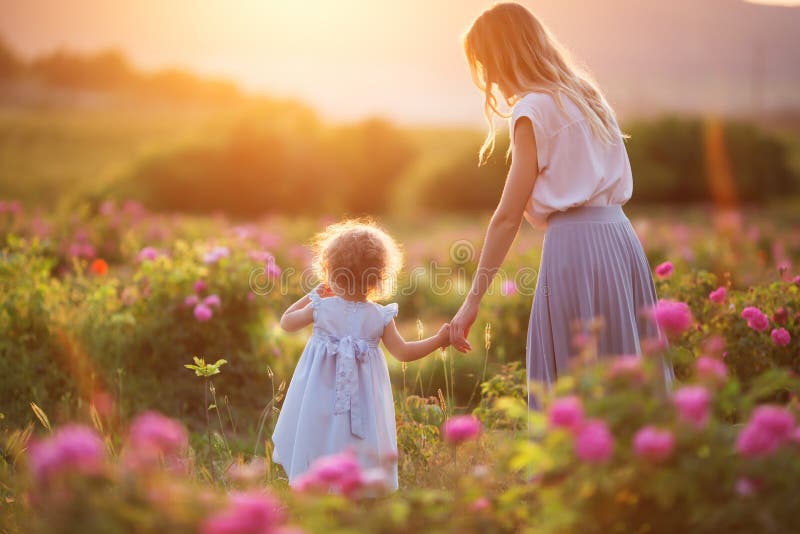 A menina da criança bonita com a mãe feliz nova está vestindo a roupa ocasional que anda no jardim de rosas sobre luzes do por do fotografia de stock royalty free A menina da criança bonita com a mãe feliz nova está vestindo a roupa ocasional que anda no jardim de rosas sobre luzes do por do fotografia de stock royalty free