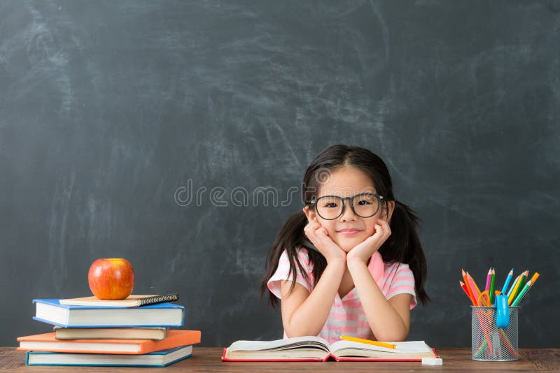 Lovely pretty little kid girl back to school sitting in class studying and face to camera smiling on blackboard background. Lovely pretty little kid girl back to school sitting in class studying and face to camera smiling on blackboard background.
