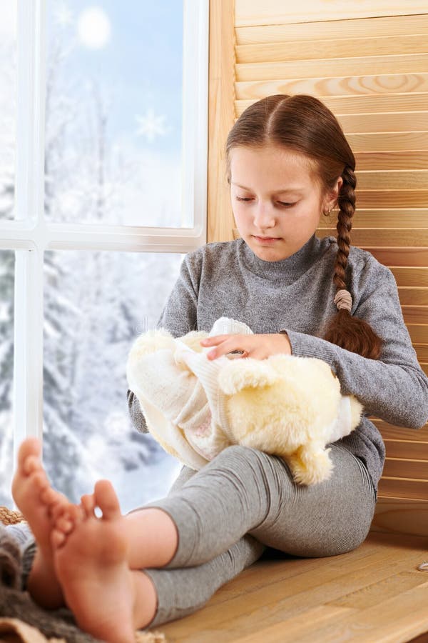 A menina da criança está sentando-se em um peitoril da janela e está jogando-se com brinquedo do urso Vista bonita fora da janela foto de stock A menina da criança está sentando-se em um peitoril da janela e está jogando-se com brinquedo do urso Vista bonita fora da janela foto de stock