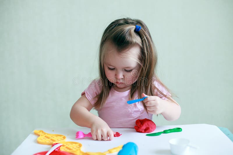 Menina da criança que senta-se na tabela que joga com a argila colorida interna, o conceito da educação pré-escolar e a terapia d imagem de stock Menina da criança que senta-se na tabela que joga com a argila colorida interna, o conceito da educação pré-escolar e a terapia d imagem de stock