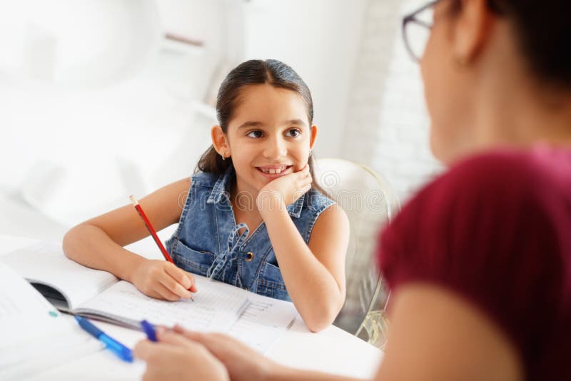 Menina de ajuda da mãe latino-americano que faz trabalhos de casa da escola em casa foto de stock Menina de ajuda da mãe latino-americano que faz trabalhos de casa da escola em casa foto de stock