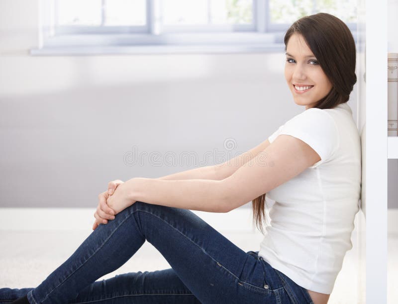 Menina de faculdade feliz que senta-se no assoalho imagem de stock Menina de faculdade feliz que senta-se no assoalho imagem de stock