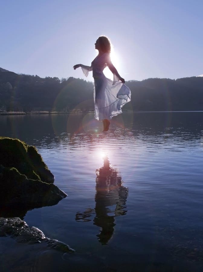 A menina de flutuação bonita vestiu-se no branco, mostrado em silhueta pelo sol refletido no lago imóvel fotos de stock royalty free A menina de flutuação bonita vestiu-se no branco, mostrado em silhueta pelo sol refletido no lago imóvel fotos de stock royalty free