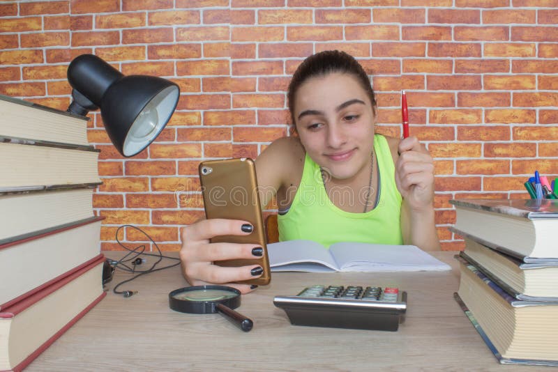 Menina de sorriso do adolescente que faz trabalhos de casa na tabela em casa Estudante com a pilha dos livros e das notas que est fotografia de stock royalty free Menina de sorriso do adolescente que faz trabalhos de casa na tabela em casa Estudante com a pilha dos livros e das notas que est fotografia de stock royalty free