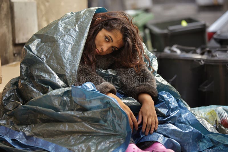 Poor girl in city sitting in street near bin. Poor girl in city sitting in street near bin