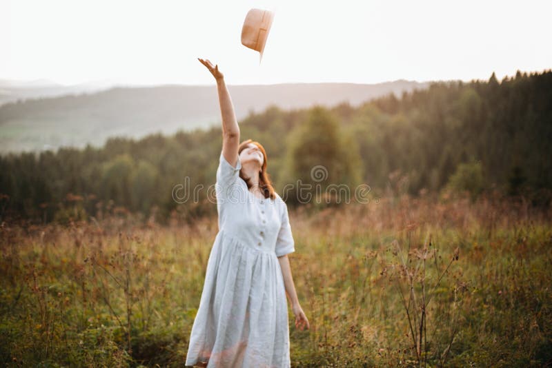 Menina despreocupada à moda do boho que joga seu chapéu no céu na luz ensolarada no por do sol atmosférico Mulher feliz do modern imagem de stock royalty free Menina despreocupada à moda do boho que joga seu chapéu no céu na luz ensolarada no por do sol atmosférico Mulher feliz do modern imagem de stock royalty free
