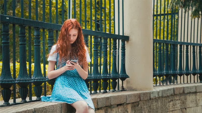 A menina do ruivo do gengibre olha no telefone fotos de stock royalty free A menina do ruivo do gengibre olha no telefone fotos de stock royalty free