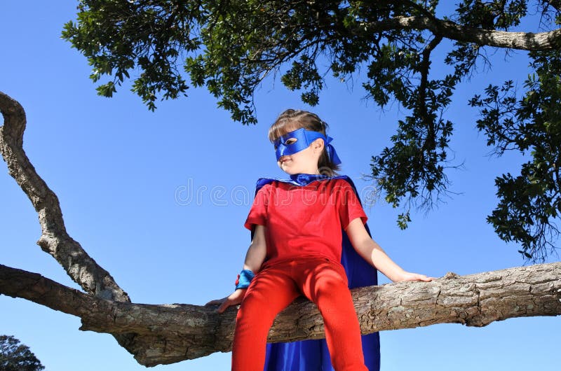 A menina do super-herói senta-se em uma árvore foto de stock royalty free