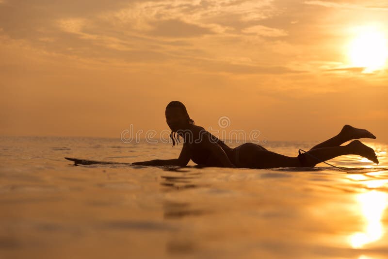 Surfer girl waiting in the line up for a wave at sunrise or sunset. Surfer girl waiting in the line up for a wave at sunrise or sunset