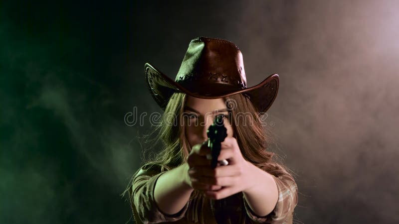 A menina do xerife guarda um revólver em suas mãos e em visar o bandido Fundo preto do fumo Movimento lento