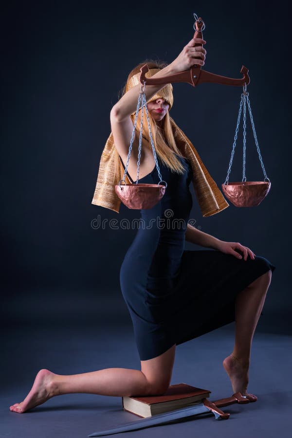 A menina, dobrando um joelho no livro com uma espada, guarda a Libra à disposição como Themis imagem de stock A menina, dobrando um joelho no livro com uma espada, guarda a Libra à disposição como Themis imagem de stock