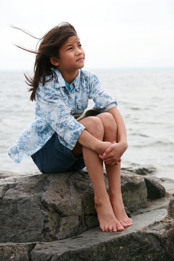 Menina dos anos de idade nove que senta-se pelo lago