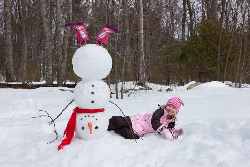 4-5 years old girl lying down next to a snowman. 4-5 years old girl lying down next to a snowman