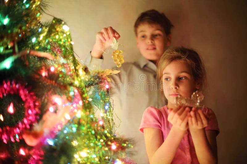 A menina e o menino decoraram a árvore de Natal pelos brinquedos de vidro na noite. imagens de stock royalty free A menina e o menino decoraram a árvore de Natal pelos brinquedos de vidro na noite. imagens de stock royalty free