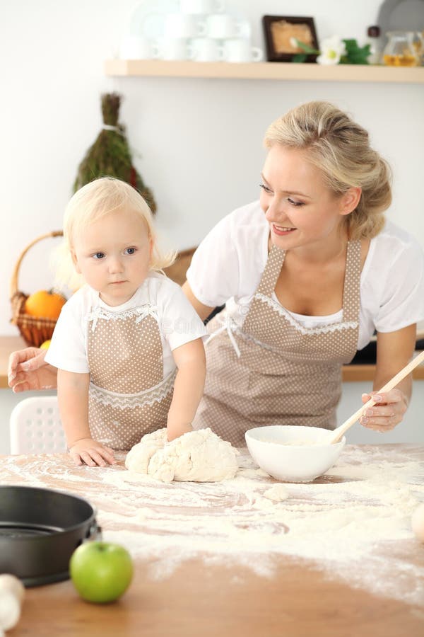 Menina e sua mam? loura nos aventais bege que jogam e que riem ao amassar a massa na cozinha Pastelaria caseiro fotografia de stock royalty free Menina e sua mam? loura nos aventais bege que jogam e que riem ao amassar a massa na cozinha Pastelaria caseiro fotografia de stock royalty free