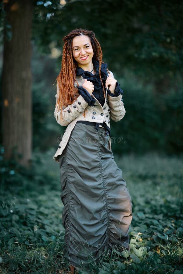 Menina elegante dos dreadlocks felizes que levanta na floresta foto de stock royalty free Menina elegante dos dreadlocks felizes que levanta na floresta foto de stock royalty free