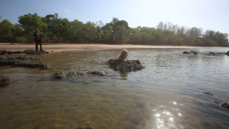 A menina em dissipadores do roupa de banho no guitarrista do mar olha e joga