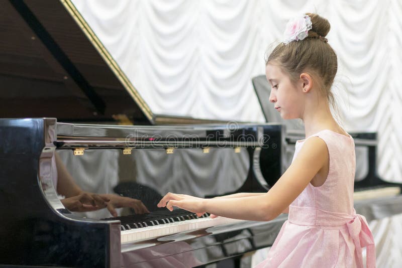 menina em um vestido cor-de-rosa bonito que joga em um piano de cauda preto Menina que joga em um piano preto fotografia de stock menina em um vestido cor-de-rosa bonito que joga em um piano de cauda preto Menina que joga em um piano preto fotografia de stock