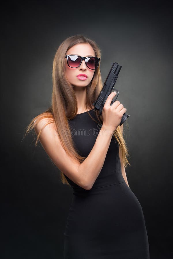 Menina em um vestido preto e nos óculos de sol que guardam uma arma foto de stock royalty free Menina em um vestido preto e nos óculos de sol que guardam uma arma foto de stock royalty free
