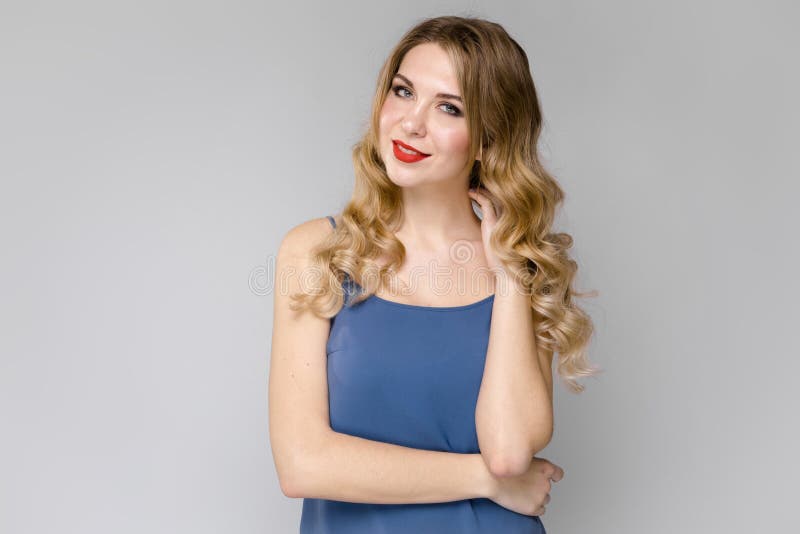 Menina encantador com cabelo encaracolado longo branco Menina em uma parte superior azul em um fundo claro foto de stock royalty free Menina encantador com cabelo encaracolado longo branco Menina em uma parte superior azul em um fundo claro foto de stock royalty free