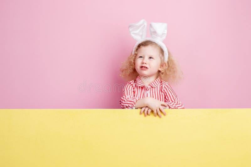 Menina encaracolado pequena engraçada em umas orelhas vermelhas e brancas listradas do vestido e do coelho em seus suportes princ fotos de stock Menina encaracolado pequena engraçada em umas orelhas vermelhas e brancas listradas do vestido e do coelho em seus suportes princ fotos de stock