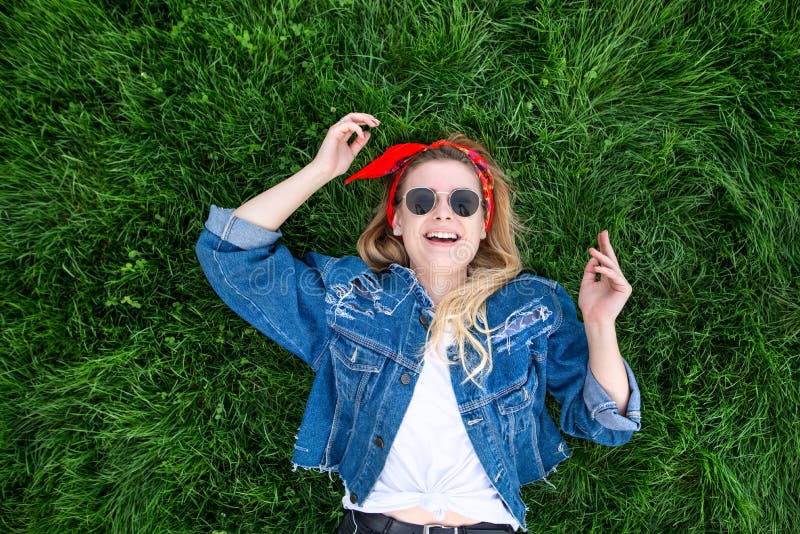 A menina encontra-se em um gramado verde, olhares na câmera e exulta-se Retrato de uma jovem mulher feliz, à moda que encontra-se fotos de stock A menina encontra-se em um gramado verde, olhares na câmera e exulta-se Retrato de uma jovem mulher feliz, à moda que encontra-se fotos de stock