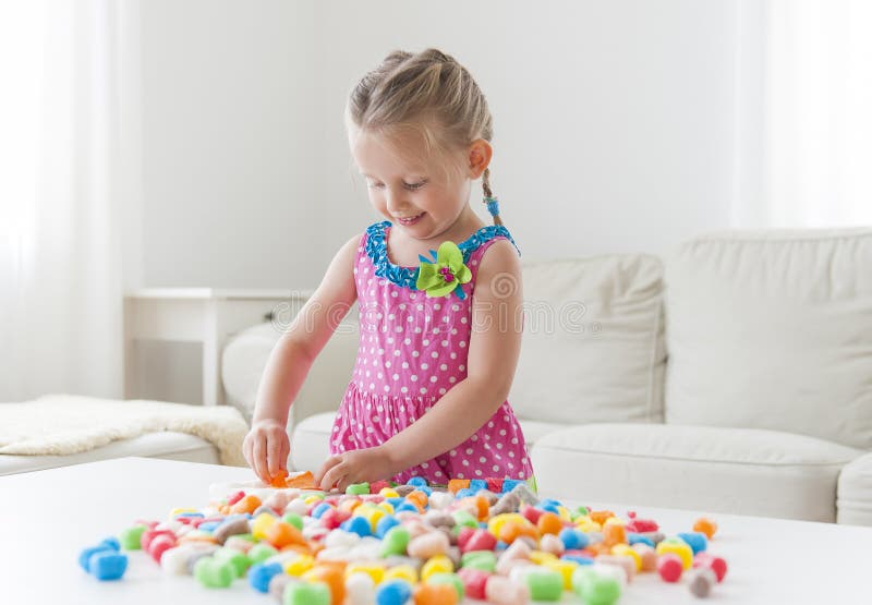 Menina engraçada bonito em um vestido colorido que joga com brinquedos coloridos Fundo brilhante fotografia de stock royalty free Menina engraçada bonito em um vestido colorido que joga com brinquedos coloridos Fundo brilhante fotografia de stock royalty free