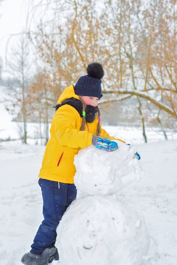 A menina esculpe o boneco de neve a criança está levando uma protuberância da neve imagens de stock royalty free A menina esculpe o boneco de neve a criança está levando uma protuberância da neve imagens de stock royalty free