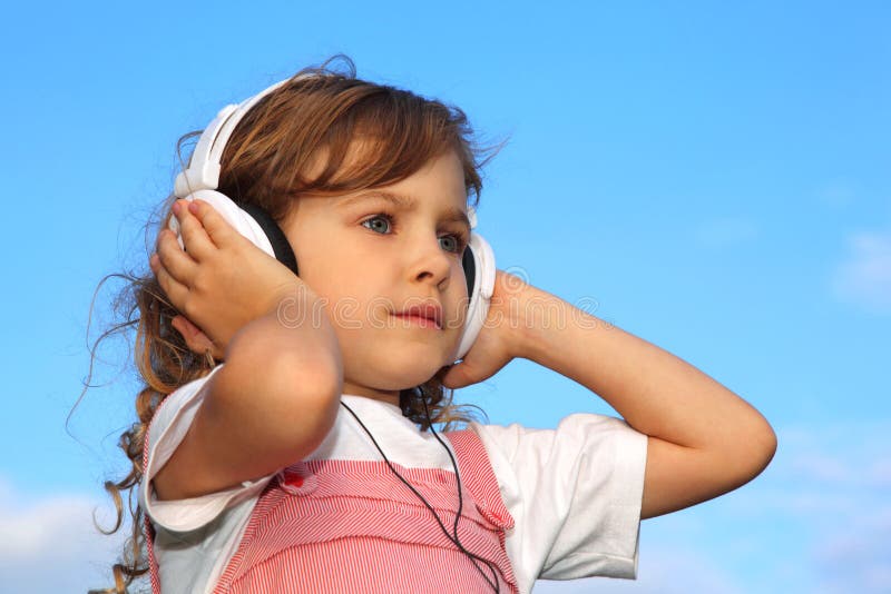 A menina escuta a música através dos fones de ouvido imagens de stock A menina escuta a música através dos fones de ouvido imagens de stock