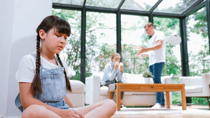 Stressed and unhappy young girl huddle in corner, cover her ears blocking sound of her parent arguing in background. Domestic violence at home and traumatic childhood develop to depression. Synchronos. Stressed and unhappy young girl huddle in corner, cover her ears blocking sound of her parent arguing in background. Domestic violence at home and traumatic childhood develop to depression. Synchronos