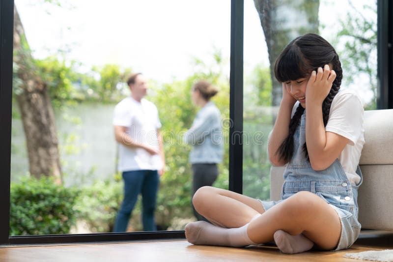 Stressed and unhappy young girl huddle in corner, cover her ears blocking sound of her parent arguing in background. Domestic violence at home and traumatic childhood develop to depression. Synchronos. Stressed and unhappy young girl huddle in corner, cover her ears blocking sound of her parent arguing in background. Domestic violence at home and traumatic childhood develop to depression. Synchronos