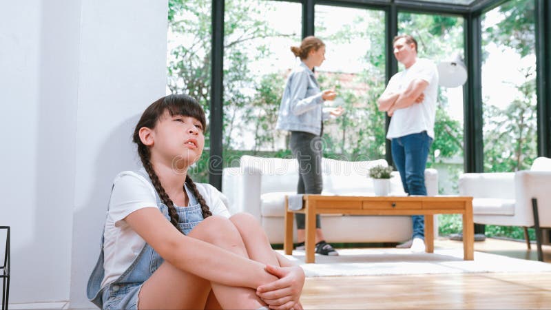 Stressed and unhappy young girl huddle in corner, cover her ears blocking sound of her parent arguing in background. Domestic violence at home and traumatic childhood develop to depression. Synchronos. Stressed and unhappy young girl huddle in corner, cover her ears blocking sound of her parent arguing in background. Domestic violence at home and traumatic childhood develop to depression. Synchronos