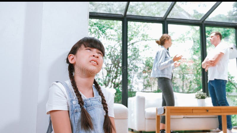 Stressed and unhappy young girl huddle in corner, cover her ears blocking sound of her parent arguing in background. Domestic violence at home and traumatic childhood develop to depression. Synchronos. Stressed and unhappy young girl huddle in corner, cover her ears blocking sound of her parent arguing in background. Domestic violence at home and traumatic childhood develop to depression. Synchronos