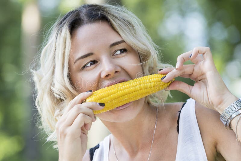 The girl is eating boiled sweet corn in the park. The girl is eating boiled sweet corn in the park