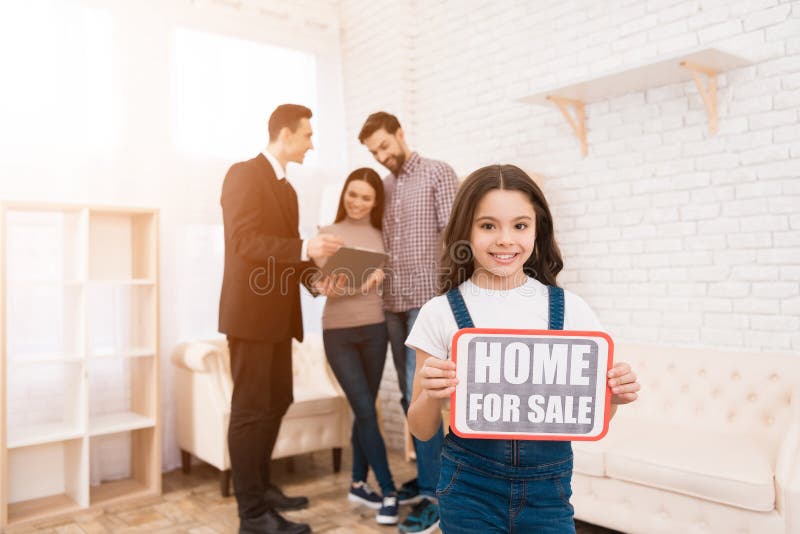 A menina está guardando o sinal com inscrição Casa para a venda O corretor de imóveis mostra o apartamento aos pares fotos de stock A menina está guardando o sinal com inscrição Casa para a venda O corretor de imóveis mostra o apartamento aos pares fotos de stock