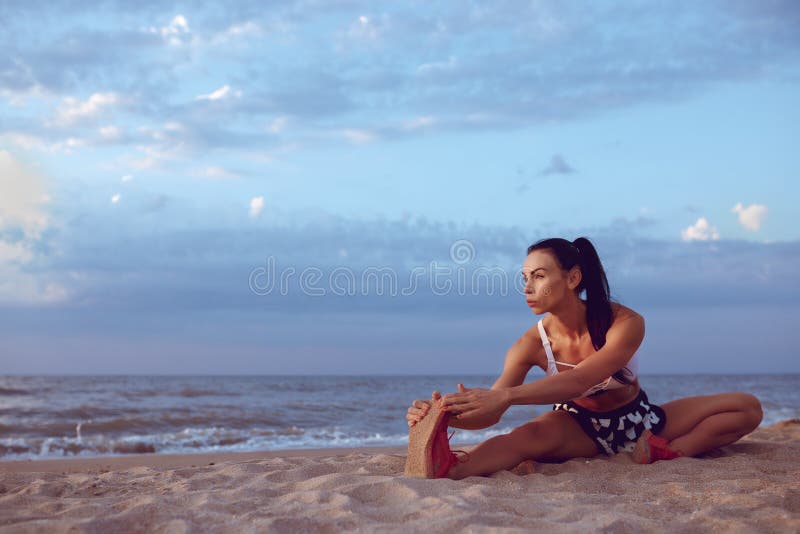 A menina faz um aquecimento antes de fazer esportes cedo na manhã no litoral Uma menina da construção atlética com uma massa seca fotografia de stock royalty free A menina faz um aquecimento antes de fazer esportes cedo na manhã no litoral Uma menina da construção atlética com uma massa seca fotografia de stock royalty free